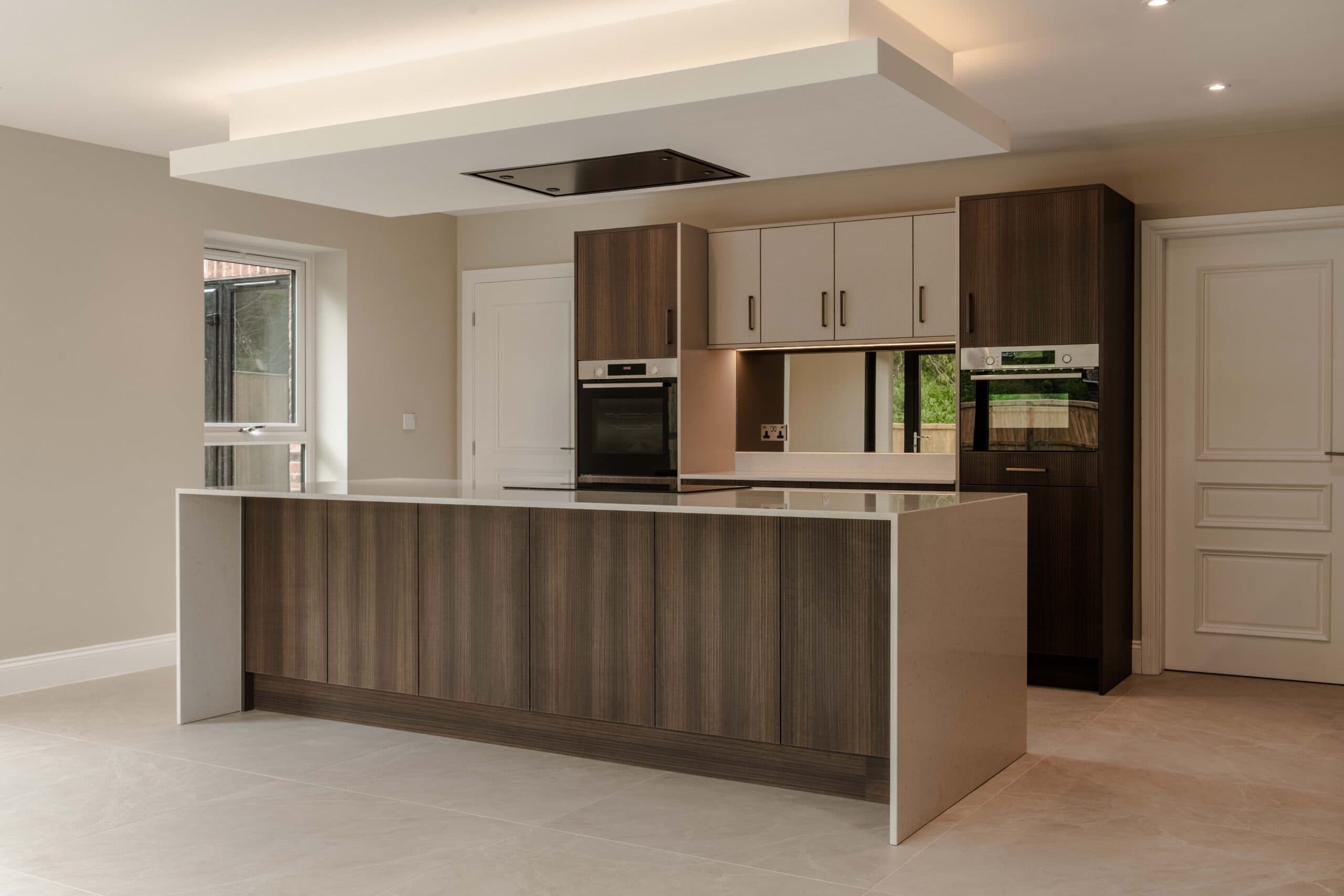 Kitchen with a dark wood island, white waterfall worktop and built-in ovens