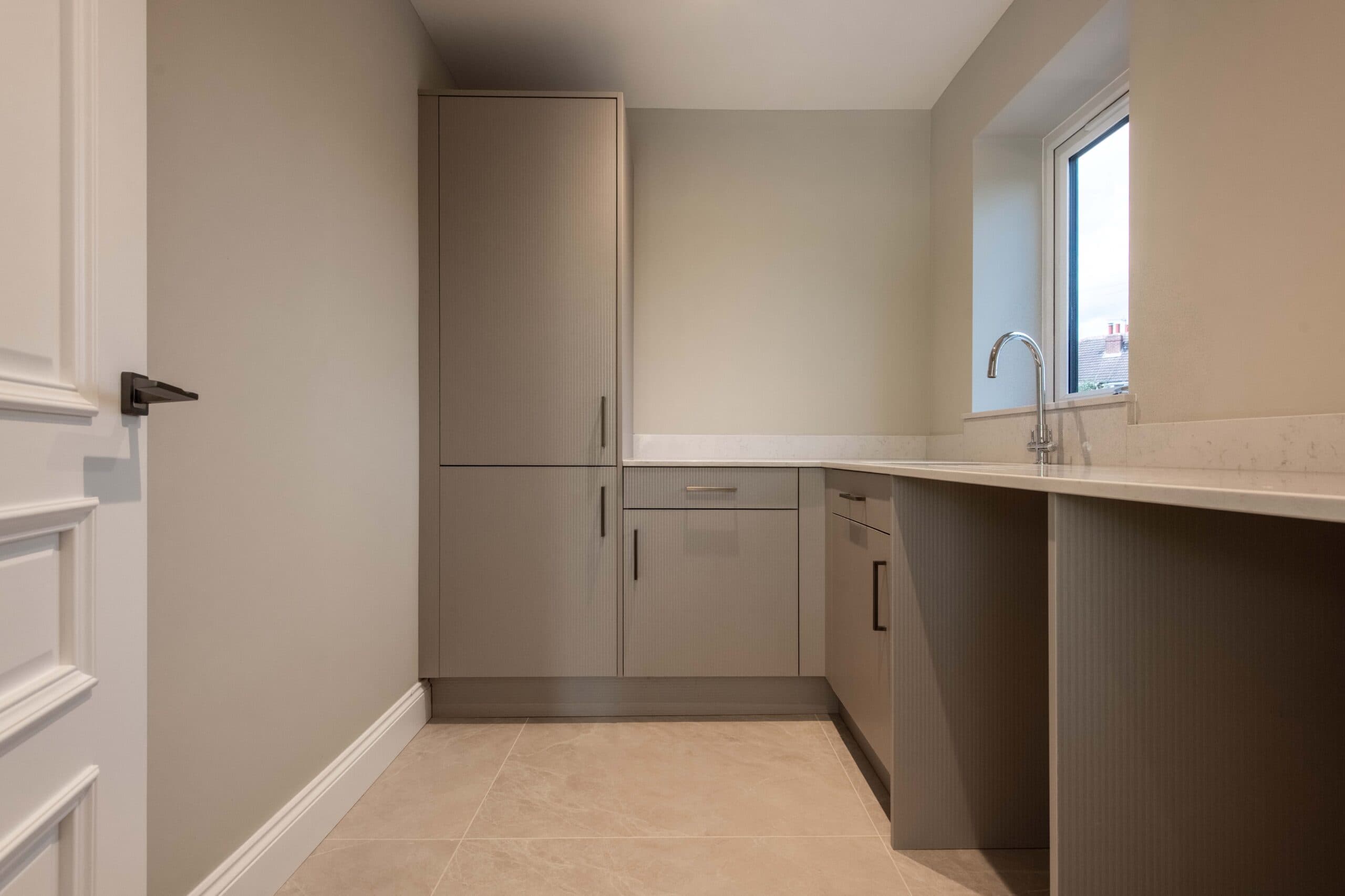 Utility room with fitted units, quartz worktop and a sink under the window